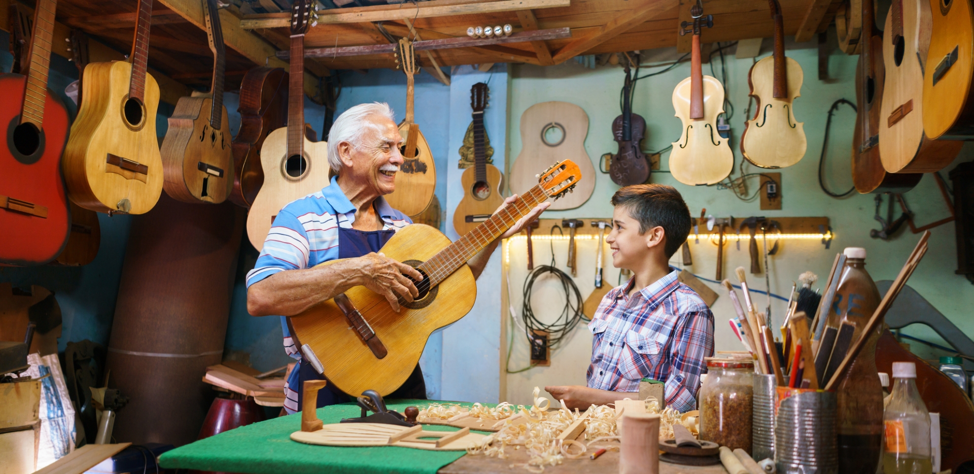 grandfather teaches adolescent grandson how to make a guitar in their wood-carving workshop